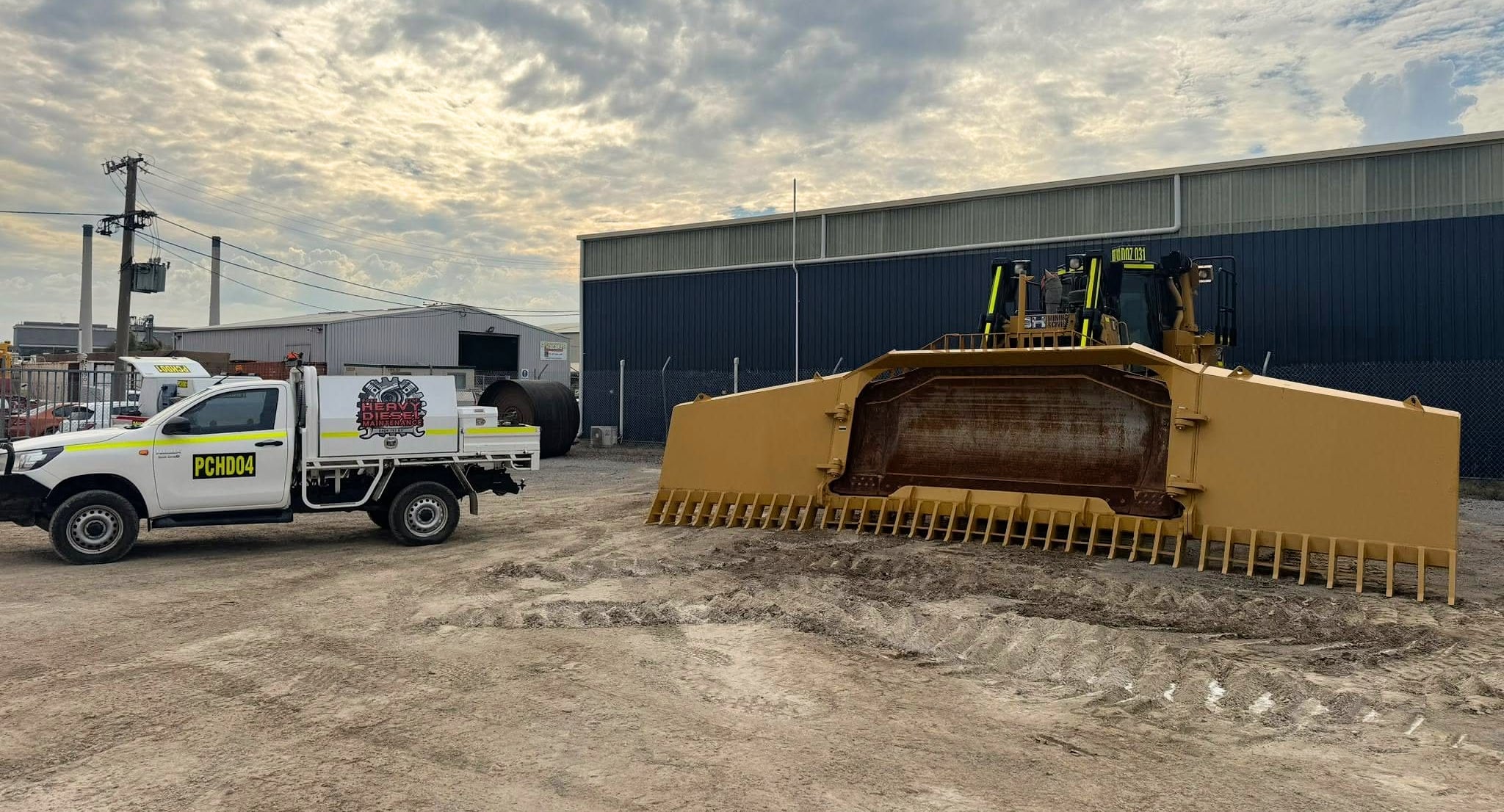 A Port City ute beside a large dozer blade outside a workshop