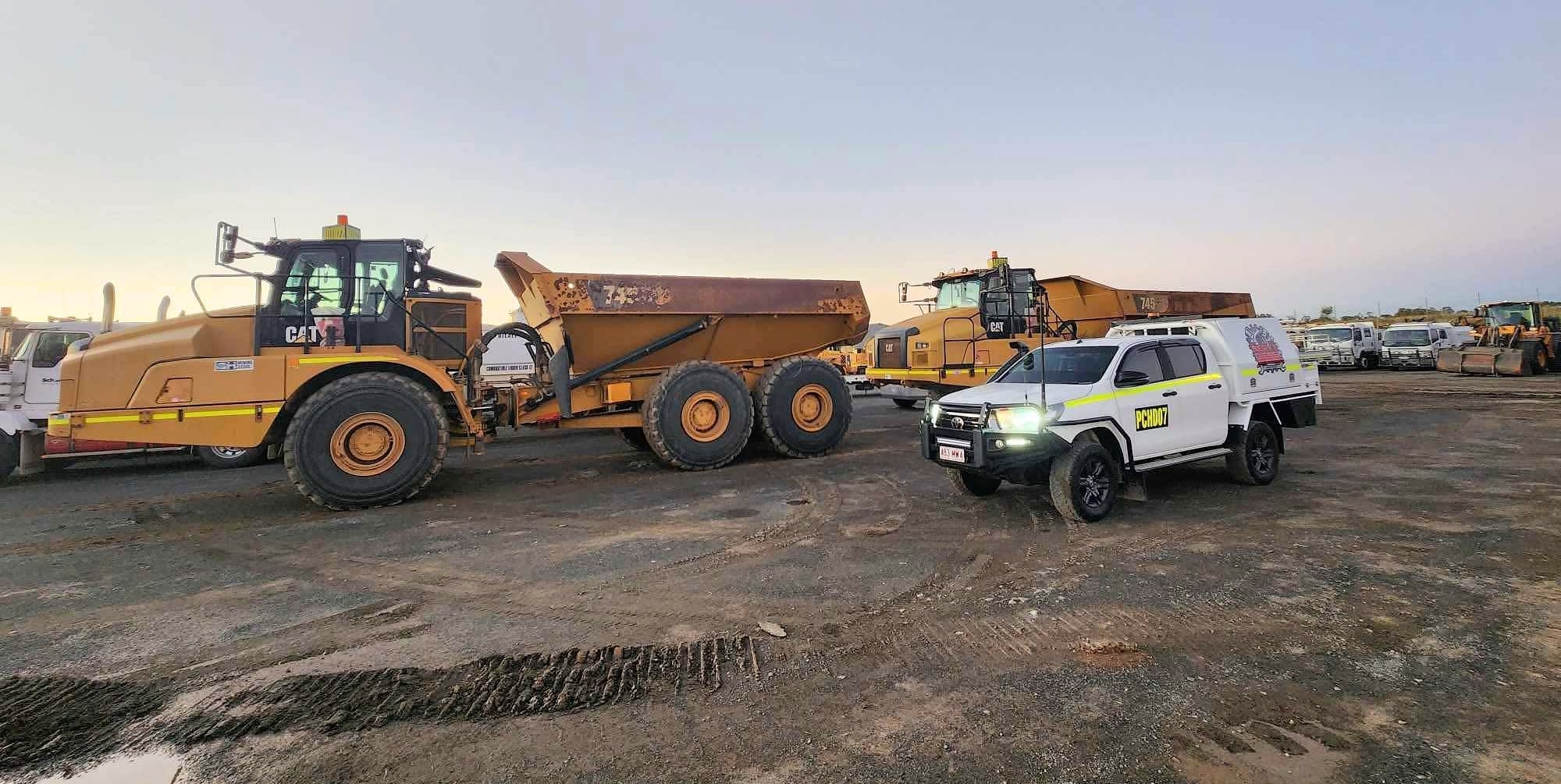 Two Caterpillar articulated dump trucks and a Port City ute on site at dusk