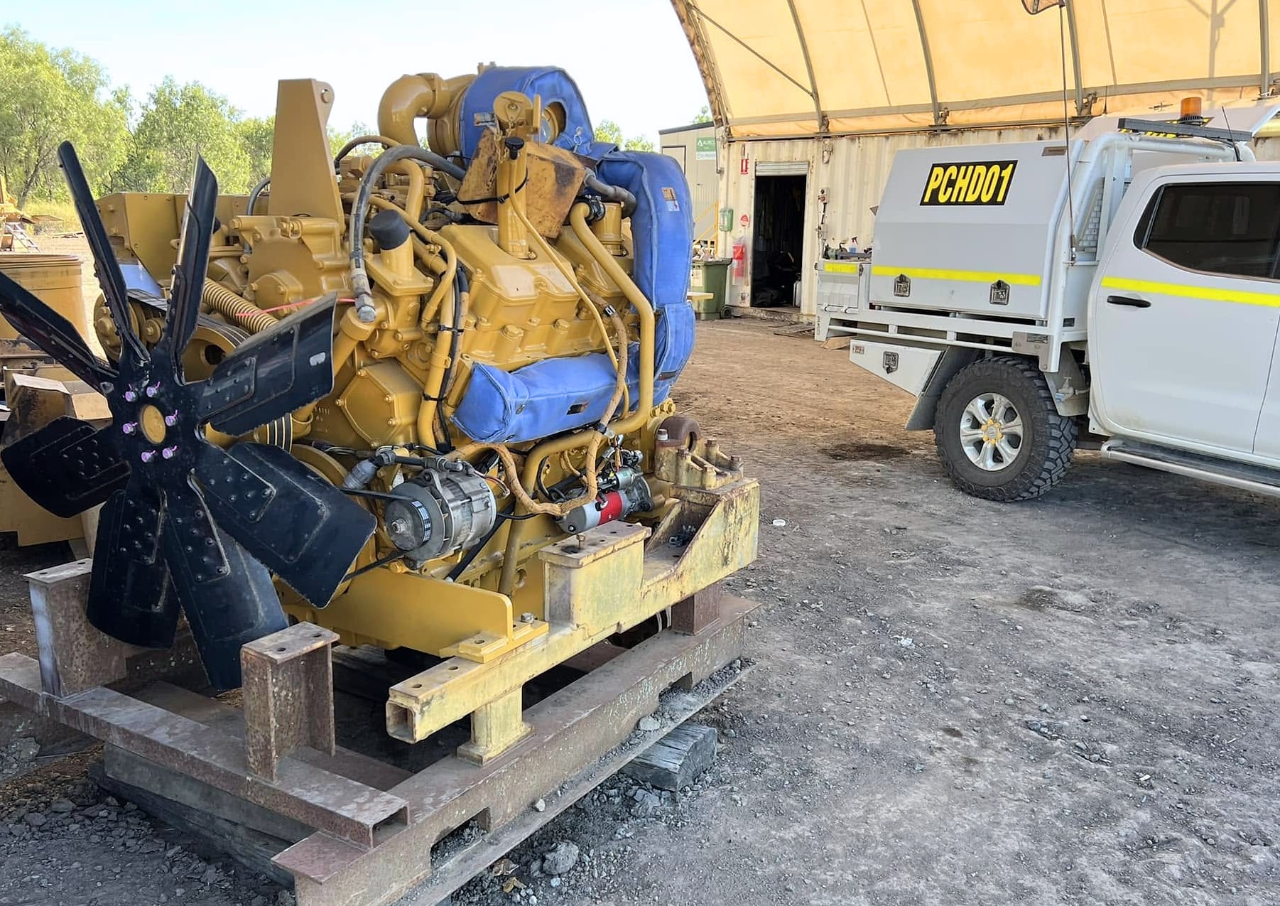 A diesel engine on a skid in the yard, beside a Port City ute