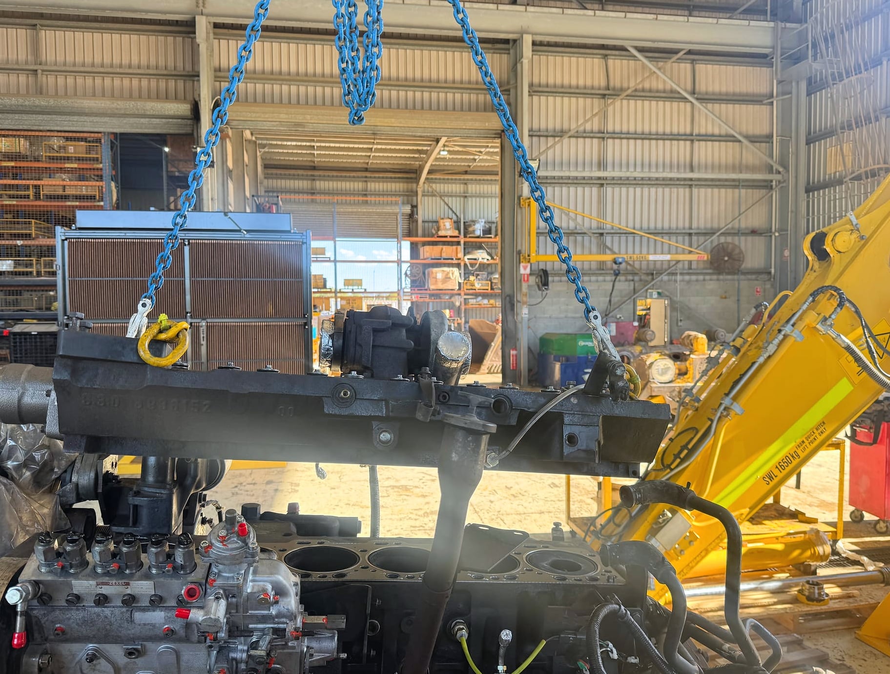 A Komatsu diesel engine opened up in the workshop, with a cylinder head lifted clear on chains