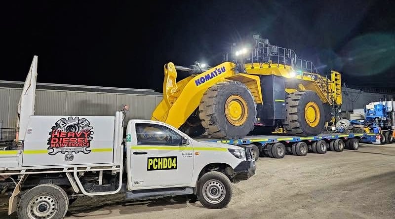 A Komatsu wheel loader on a float at night, with a Port City service ute in front