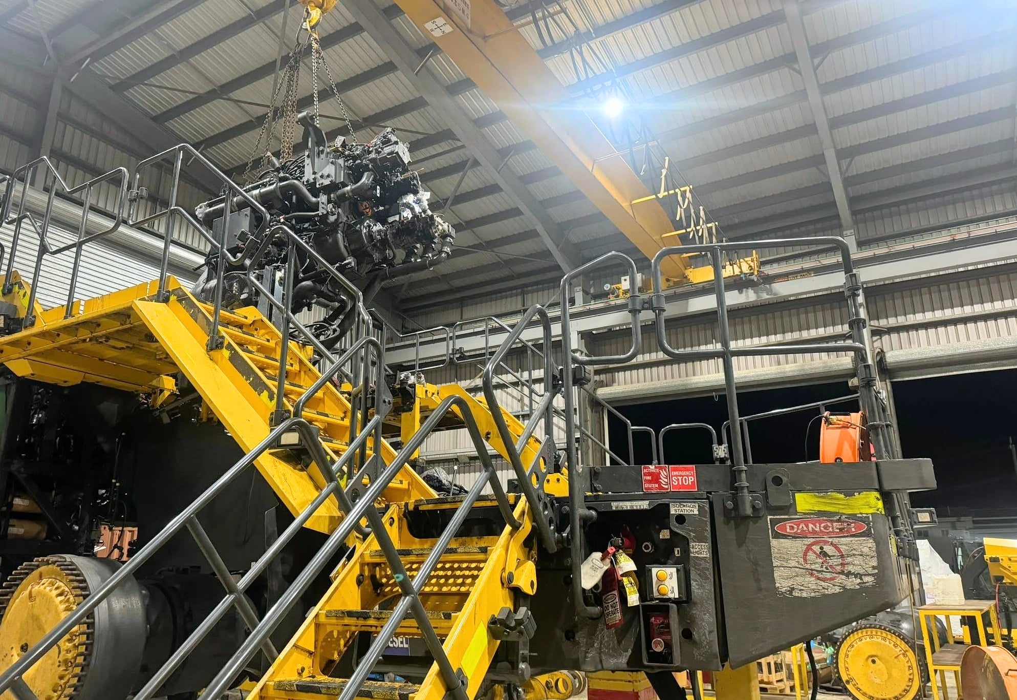 A wheel loader mid-rebuild, with a major component lifted clear on the workshop crane
