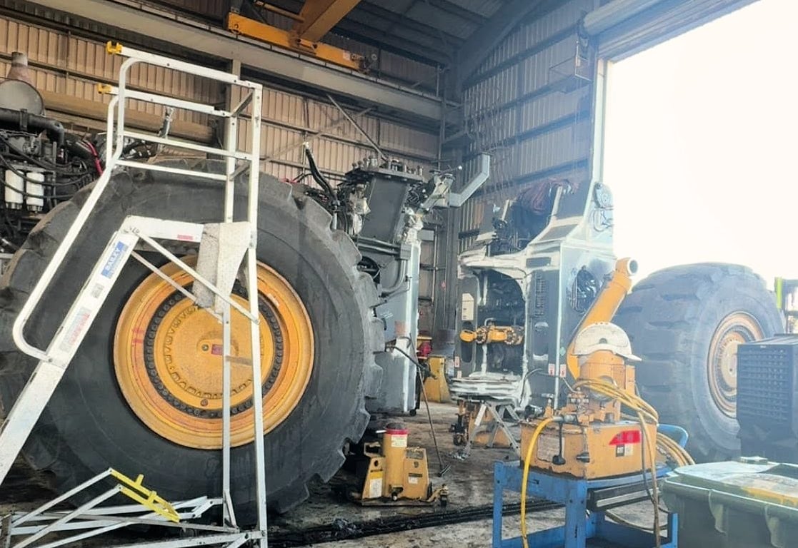 A wheel loader stripped down under an overhead crane in the workshop